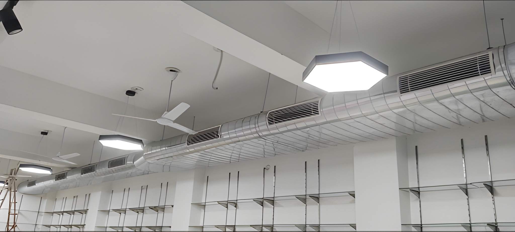 Large-diameter spiral circular duct with side rectangular supply grilles in modern showroom